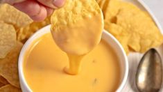 a person dipping cheese into a bowl of tortilla chips with a spoon in it