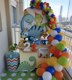 a birthday party with balloons and decorations on the table in front of a large window