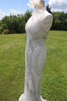 a white dress with feathers on it is standing in the middle of a grassy field