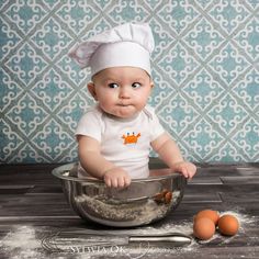 a baby in a chef's hat sitting in a bowl with eggs on the floor