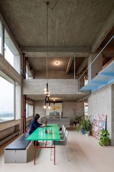 a person sitting at a green table in a room with high ceilings and large windows