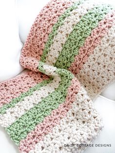 a crocheted blanket is laying on a white couch with a green and pink striped afghan