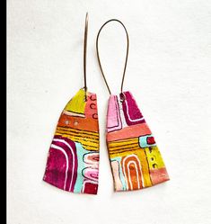 two pairs of colorful wooden earrings with metal hooks hanging from them on a white surface