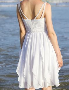 a woman in a white dress standing on the beach looking out at the ocean with her back to the camera