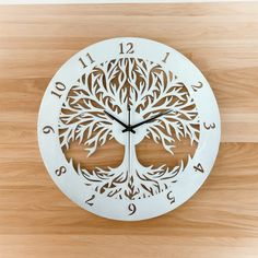 a white clock with a tree cut out of it's face on a wooden surface