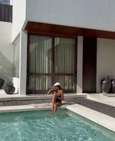 a woman sitting on the edge of a swimming pool in front of a white building