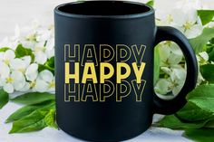 a black coffee mug with the words happy on it next to some white and green flowers