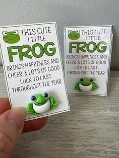 someone is holding two little frog brooches in front of their earring cards