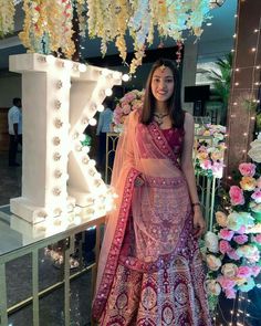 a woman in a pink and gold lehenga standing next to a flower display