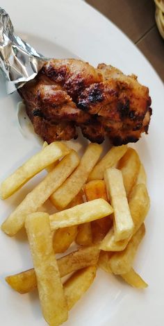 a white plate topped with chicken and french fries next to a piece of tin foil