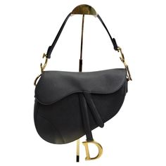 Introducing the Christian Dior Medium Saddle Bag in Black Calfskin, a timeless icon of luxury fashion. Crafted from grained calfskin leather in the iconic saddle shape, this bag exudes sophistication and elegance. The bag features gold-tone CD logos on the sides, adding a touch of signature Dior flair. The gold-tone hardware and dangling D charm on the flap further elevate the design, exuding opulence and refinement. Secured with a magnetic closure, the bag opens to reveal a spacious interior, p Luxury Black Saddle Bag For Evening, Luxury Saddle Bag With Gold-tone Hardware, Luxury Black Saddle Bag With Detachable Handle, Designer Saddle Shoulder Bag For Evening, Evening Saddle Bag With Gold-tone Hardware, Designer Saddle Bag With Leather Lining, Designer Saddle Bag For Formal Events, Elegant Evening Saddle Bag, Luxury Leather Saddle Bag With Horsebit Detail