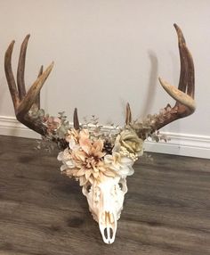 a deer skull with flowers on it's antlers sitting on a wooden floor