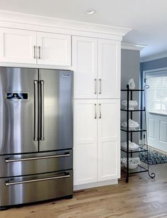 a stainless steel refrigerator in a kitchen with white cabinets and wood flooring on the side