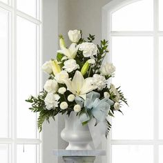 a vase filled with white flowers sitting on top of a table next to a window