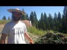 a man wearing a cowboy hat standing next to a pile of dirt and trees in the background