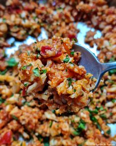 a spoon full of food that is on top of a plate with rice and vegetables