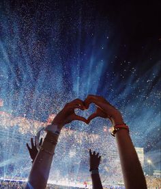 two people making a heart shape with their hands in the air at an outdoor concert