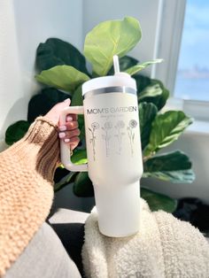 a person holding a white coffee cup with plants on it