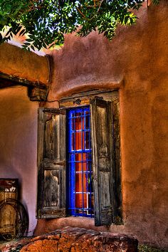 an old adobe building with a blue window and wooden shutters on the outside wall