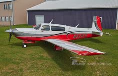 a red and silver plane parked in front of a building on the grass next to some buildings