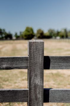 a bird perched on the top of a wooden fence in front of an open field