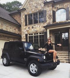 a woman sitting on the hood of a black jeep in front of a brick house