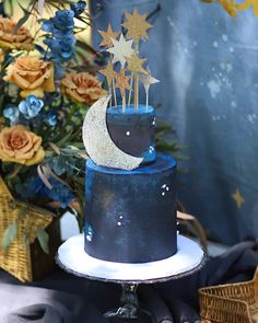 a blue and white cake with stars on top sitting on a table next to flowers