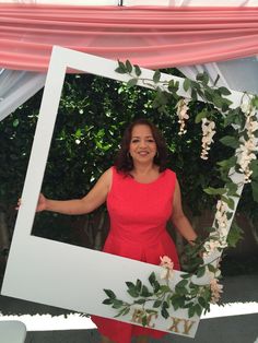 a woman in a red dress is holding up a white frame with flowers on it