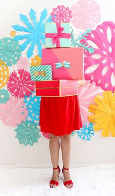 a woman in red dress holding stack of colorful boxes on her head with snowflakes behind her