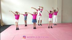 five children in pink shirts and white shorts are standing on a pink floor with their arms up