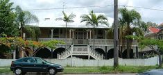 a car is parked in front of a house with palm trees on the side walk