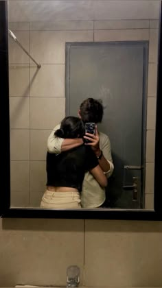 a man and woman taking a selfie in front of a bathroom mirror with their arms around each other