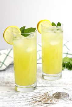 two glasses filled with lemonade on top of a white wooden table next to a towel