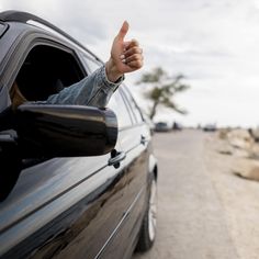 a hand sticking out the side window of a car giving a thumbs up sign to someone