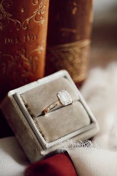 an engagement ring sitting on top of a box next to two brown book's