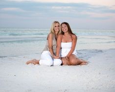 two beautiful women sitting on the beach posing for a photo with their arms around each other