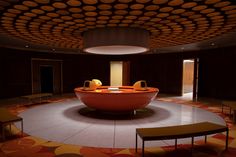 a circular room with an orange couch in the center and two tables on each side