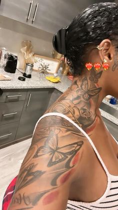 a woman with tattoos on her arm and chest sitting in a kitchen next to a counter