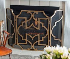 a fire place in a living room next to a chair and vase with flowers on it