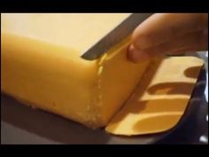 a person cutting cheese with a knife on top of the board and it is yellow