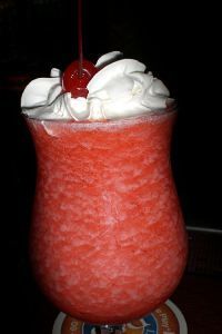 a red drink with whipped cream and a cherry on top