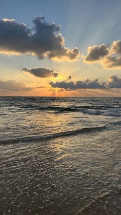 the sun is setting over the ocean with clouds in the sky and waves on the beach