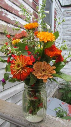 a mason jar filled with lots of flowers on top of a wooden table next to a house