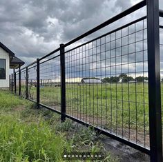 a black metal fence is in front of a white house and green grass on a cloudy day