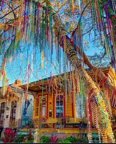 a tree with beads hanging from it's branches in front of a yellow house