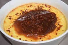 a white bowl filled with food and sauce on top of a gray countertop next to a cup of coffee