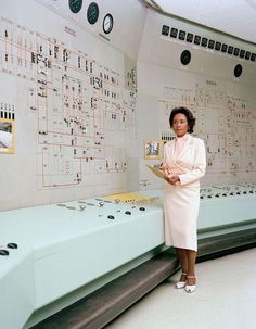 a woman standing in front of a control room with lots of buttons on the wall