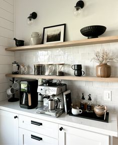 a coffee maker on top of a white counter next to some shelves filled with cups and saucers