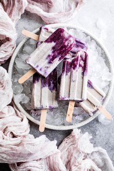 three popsicles with blue and white toppings on top of ice cubes in a bowl