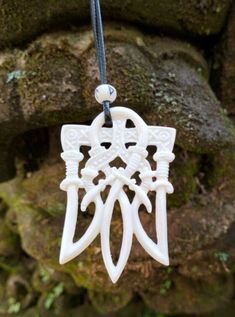 a white necklace with an intricate design on the front and back of it, hanging from a leather cord